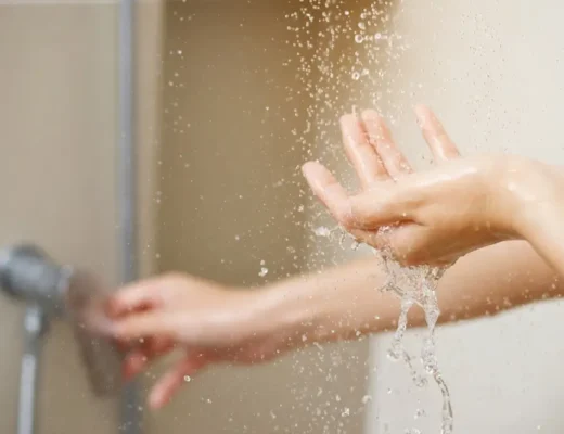 Une femme utilise la main pour mesurer la température de l'eau d'un chauffe-eau avant de prendre une douche.